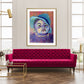 Baby boy in blue hat in colours purple, pink and  blue in gold frame. In room with bright pink sofa with gold toned furniture
